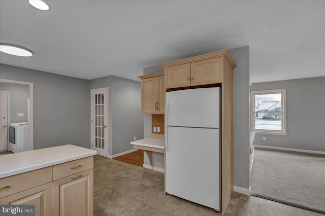 kitchen featuring light countertops, light brown cabinetry, freestanding refrigerator, washer and dryer, and baseboards