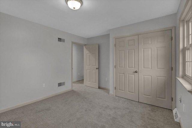 unfurnished bedroom with light colored carpet, a closet, visible vents, and baseboards