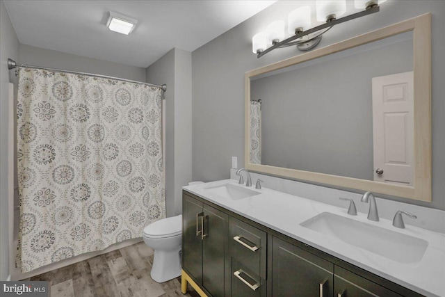 bathroom featuring wood finished floors, a sink, toilet, and double vanity