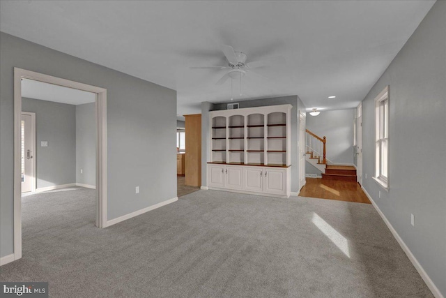 unfurnished living room with a ceiling fan, light carpet, stairway, and baseboards