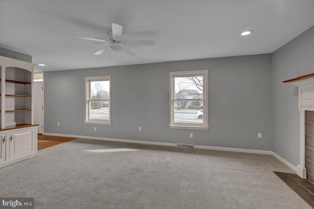 unfurnished living room featuring dark carpet, a fireplace, visible vents, and baseboards