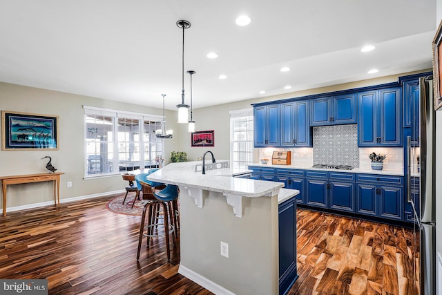 kitchen featuring light stone counters, a kitchen island with sink, blue cabinetry, appliances with stainless steel finishes, and a kitchen bar