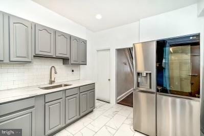 kitchen featuring gray cabinets, a sink, decorative backsplash, light countertops, and stainless steel fridge