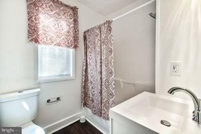 bathroom with toilet, wood finished floors, shower / tub combo, baseboards, and vanity