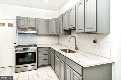 kitchen with under cabinet range hood, stainless steel gas stove, gray cabinets, and a sink