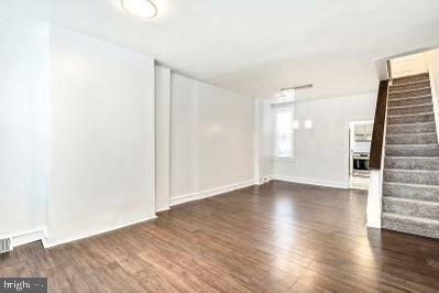 unfurnished living room with stairway, baseboards, and wood finished floors