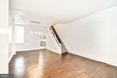 unfurnished living room featuring stairway, baseboards, and wood finished floors