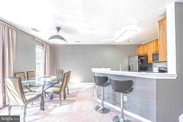 kitchen featuring a breakfast bar area, visible vents, a peninsula, appliances with stainless steel finishes, and light colored carpet