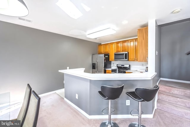 kitchen featuring light countertops, brown cabinets, a kitchen breakfast bar, appliances with stainless steel finishes, and a peninsula