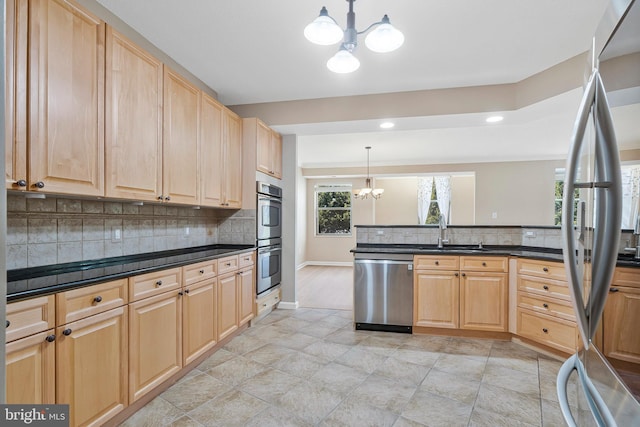 kitchen featuring pendant lighting, a notable chandelier, stainless steel appliances, dark countertops, and a sink