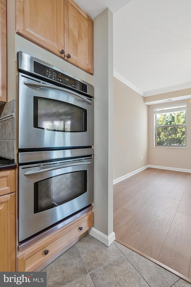 kitchen with crown molding, dark countertops, backsplash, double oven, and baseboards