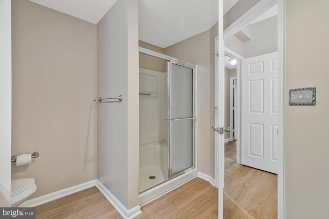 bathroom with a stall shower, wood finished floors, toilet, and baseboards