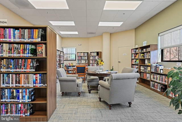 sitting room with plenty of natural light, bookshelves, carpet, and a paneled ceiling