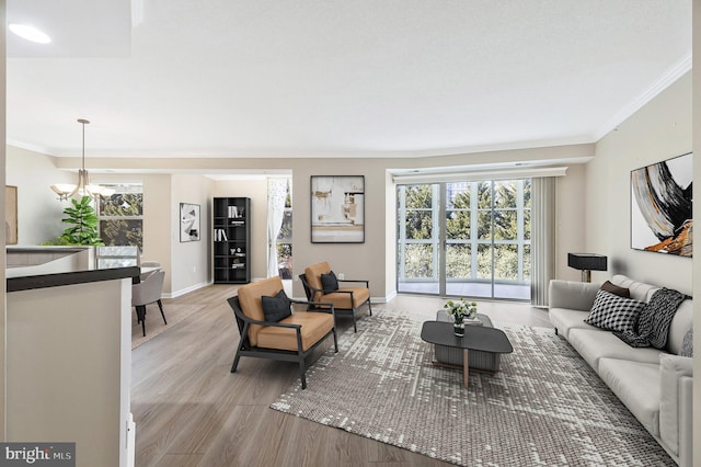 living room featuring ornamental molding, baseboards, a notable chandelier, and light wood finished floors