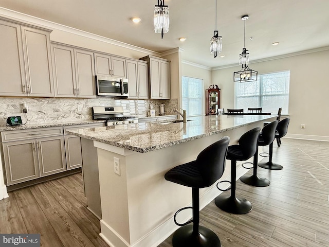 kitchen featuring light stone counters, decorative light fixtures, a center island with sink, appliances with stainless steel finishes, and backsplash