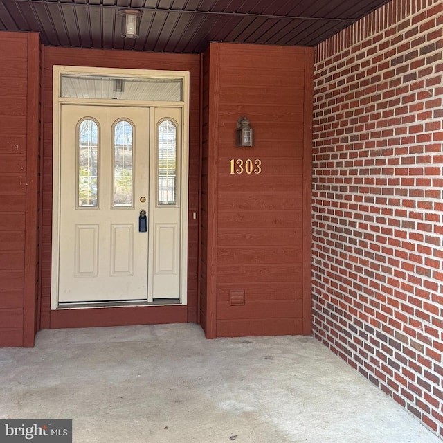 doorway to property with a porch and brick siding