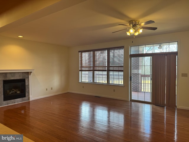 unfurnished living room with a tiled fireplace, wood finished floors, and baseboards