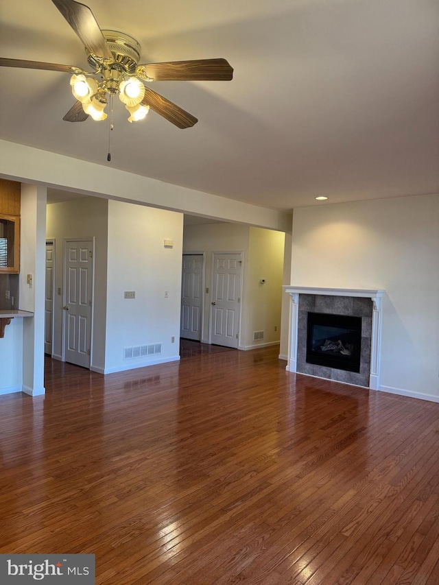 unfurnished living room featuring baseboards, visible vents, a ceiling fan, a tiled fireplace, and hardwood / wood-style flooring