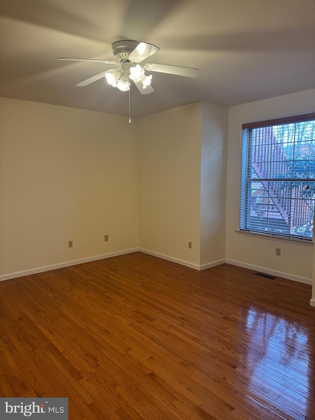 empty room with hardwood / wood-style flooring, ceiling fan, visible vents, and baseboards