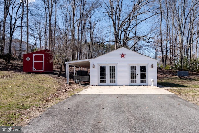 view of front facade featuring a storage unit, an outbuilding, driveway, french doors, and a carport