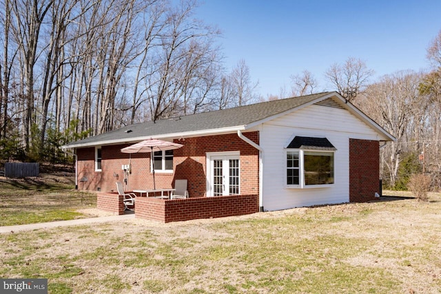 back of property featuring french doors, brick siding, and a yard