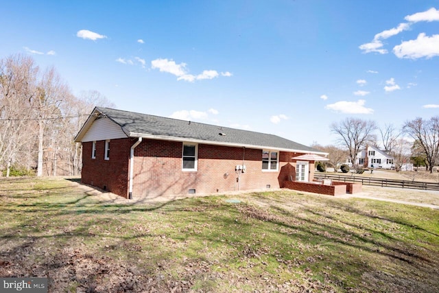 rear view of house featuring a lawn, fence, brick siding, and crawl space