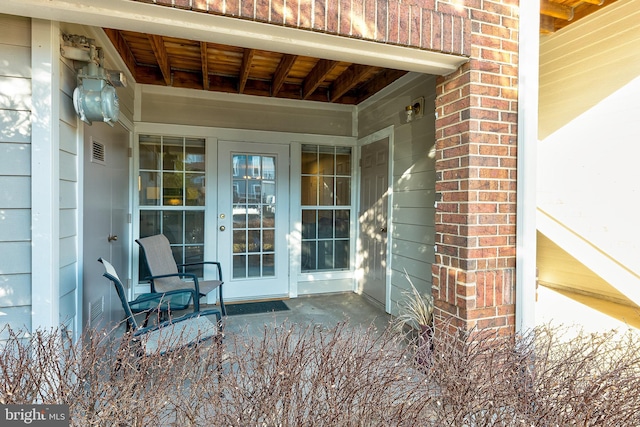 entrance to property featuring french doors, brick siding, and visible vents