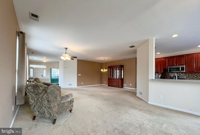 unfurnished living room featuring light carpet and ceiling fan with notable chandelier