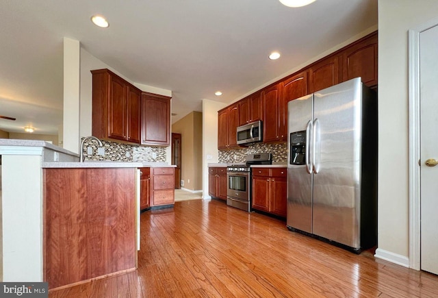 kitchen featuring tasteful backsplash, appliances with stainless steel finishes, light hardwood / wood-style flooring, and kitchen peninsula