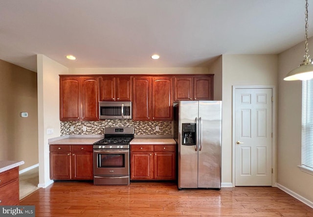 kitchen with appliances with stainless steel finishes, pendant lighting, backsplash, and light hardwood / wood-style floors