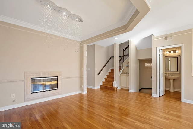 unfurnished living room with a fireplace, stairway, ornamental molding, light wood-style floors, and a sink