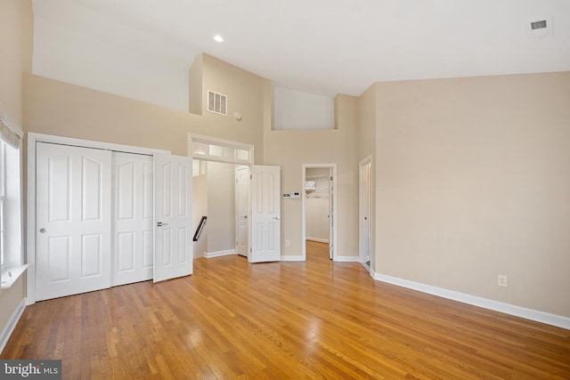 unfurnished bedroom with high vaulted ceiling, visible vents, baseboards, a closet, and light wood-type flooring