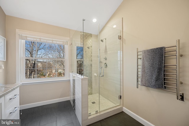 bathroom featuring lofted ceiling, radiator, a shower stall, and baseboards