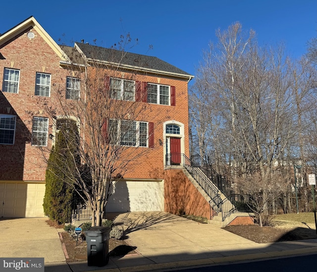 multi unit property with stairway, a garage, brick siding, and driveway