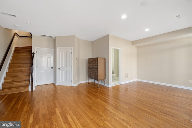 unfurnished living room with stairway, wood finished floors, visible vents, and baseboards