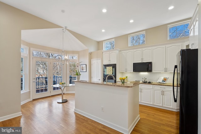 kitchen with white cabinetry, black appliances, light stone counters, and light wood-style floors