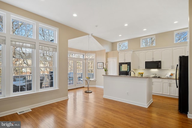 kitchen with pendant lighting, light wood finished floors, backsplash, white cabinets, and black appliances