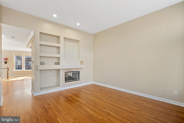 unfurnished living room with built in shelves, a glass covered fireplace, hardwood / wood-style flooring, and baseboards