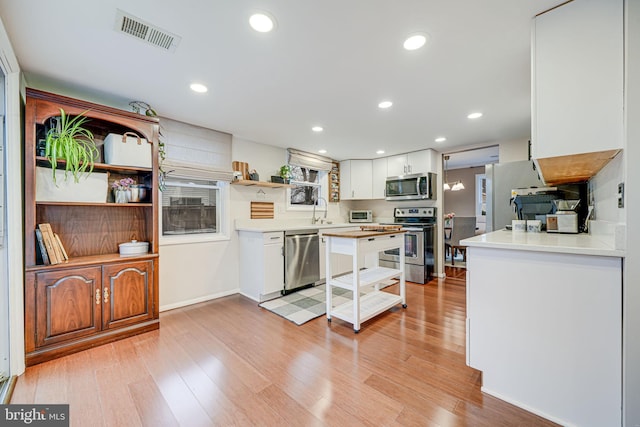 kitchen with appliances with stainless steel finishes, visible vents, light wood finished floors, and open shelves