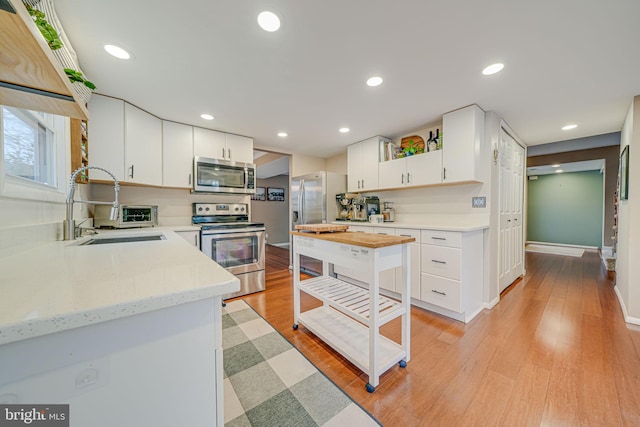 kitchen with light wood finished floors, recessed lighting, appliances with stainless steel finishes, white cabinets, and a sink