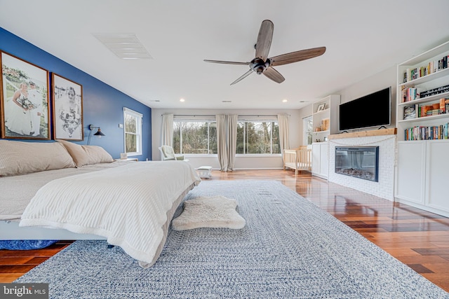 bedroom with recessed lighting, a ceiling fan, wood finished floors, and a glass covered fireplace