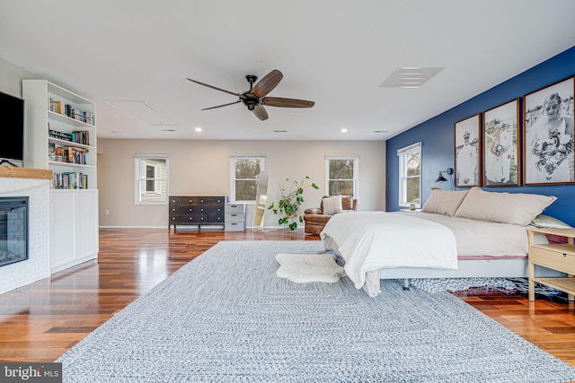 bedroom with attic access, a glass covered fireplace, visible vents, and wood finished floors