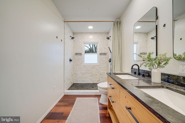 full bathroom featuring a sink, a tile shower, toilet, and wood finished floors