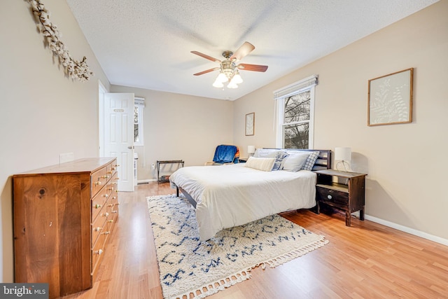 bedroom featuring light wood-type flooring, a ceiling fan, baseboards, and a textured ceiling