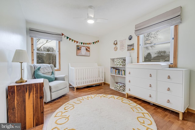 bedroom featuring ceiling fan, a crib, wood finished floors, and baseboards