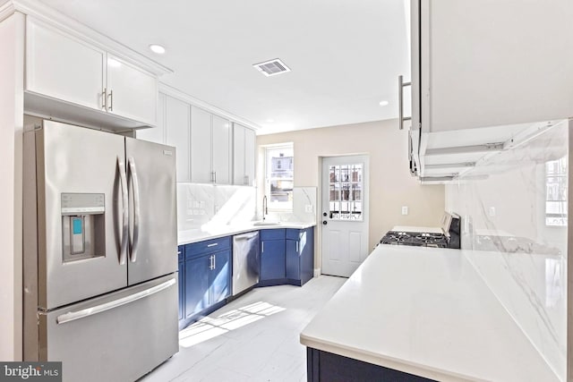 kitchen with sink, backsplash, blue cabinets, stainless steel appliances, and white cabinets