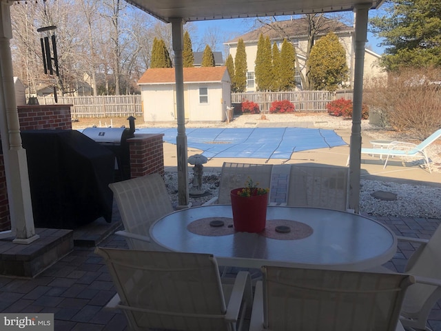 view of patio with outdoor dining space, a fenced backyard, an outdoor structure, and a storage shed