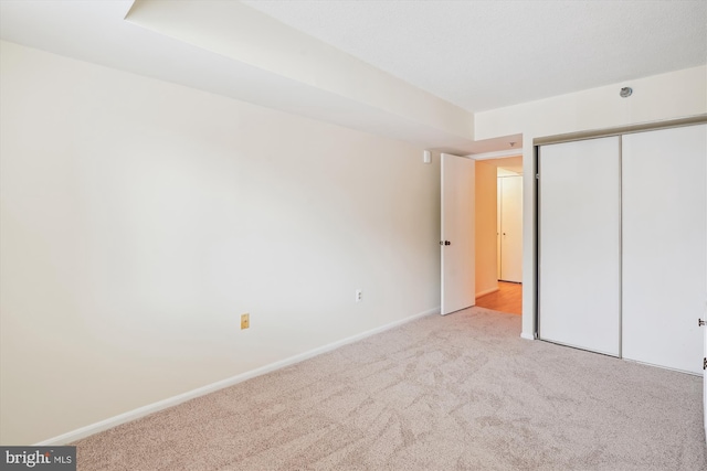 unfurnished bedroom featuring baseboards, a closet, and light colored carpet