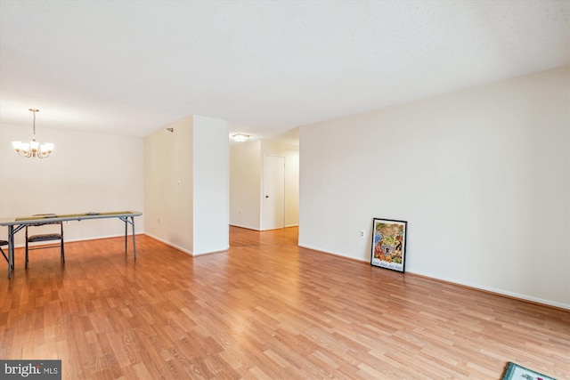 spare room with a chandelier, light wood-type flooring, and baseboards