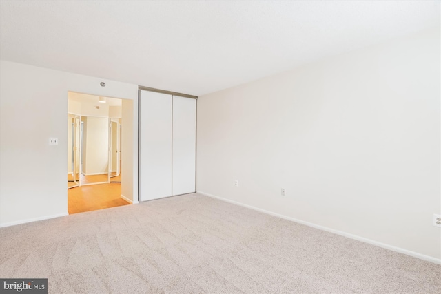 unfurnished bedroom featuring baseboards, a closet, and light colored carpet